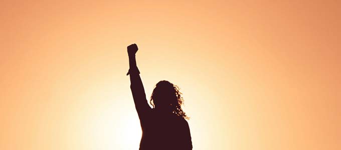 Silhouette einer Person mit erhobener Faust vor warmem Sonnenlicht